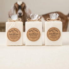 Load image into Gallery viewer, Three bars of Bass Farms Goat Milk Soap in Caramel Milk & Honey, Vanilla Rose, and Chamomile Milk scents, wrapped in clear plastic and lined up on a dark speckled granite countertop.