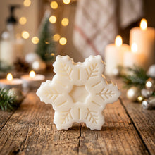 Load image into Gallery viewer, A white snowflake-shaped soap placed on a wooden surface with blurred snowflake decorations in the background.