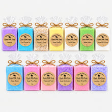 Load image into Gallery viewer, A display of various colored bars of goat milk soap, each individually wrapped with twine.