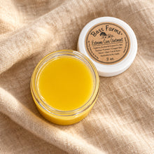Load image into Gallery viewer, An open small jar of yellow balm or ointment sits on a rustic wooden surface, with the white lid placed behind it. The lid label reads Boss Farms Extreme Skin Uplift.