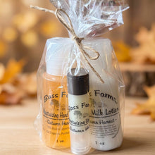 Load image into Gallery viewer, Three small artisanal skincare bottles from Bass Farms Farms, including a hand wash, a rollerball, and a milk lotion, packaged together in clear cellophane with a twine bow, set against a colorful autumn-themed background.
